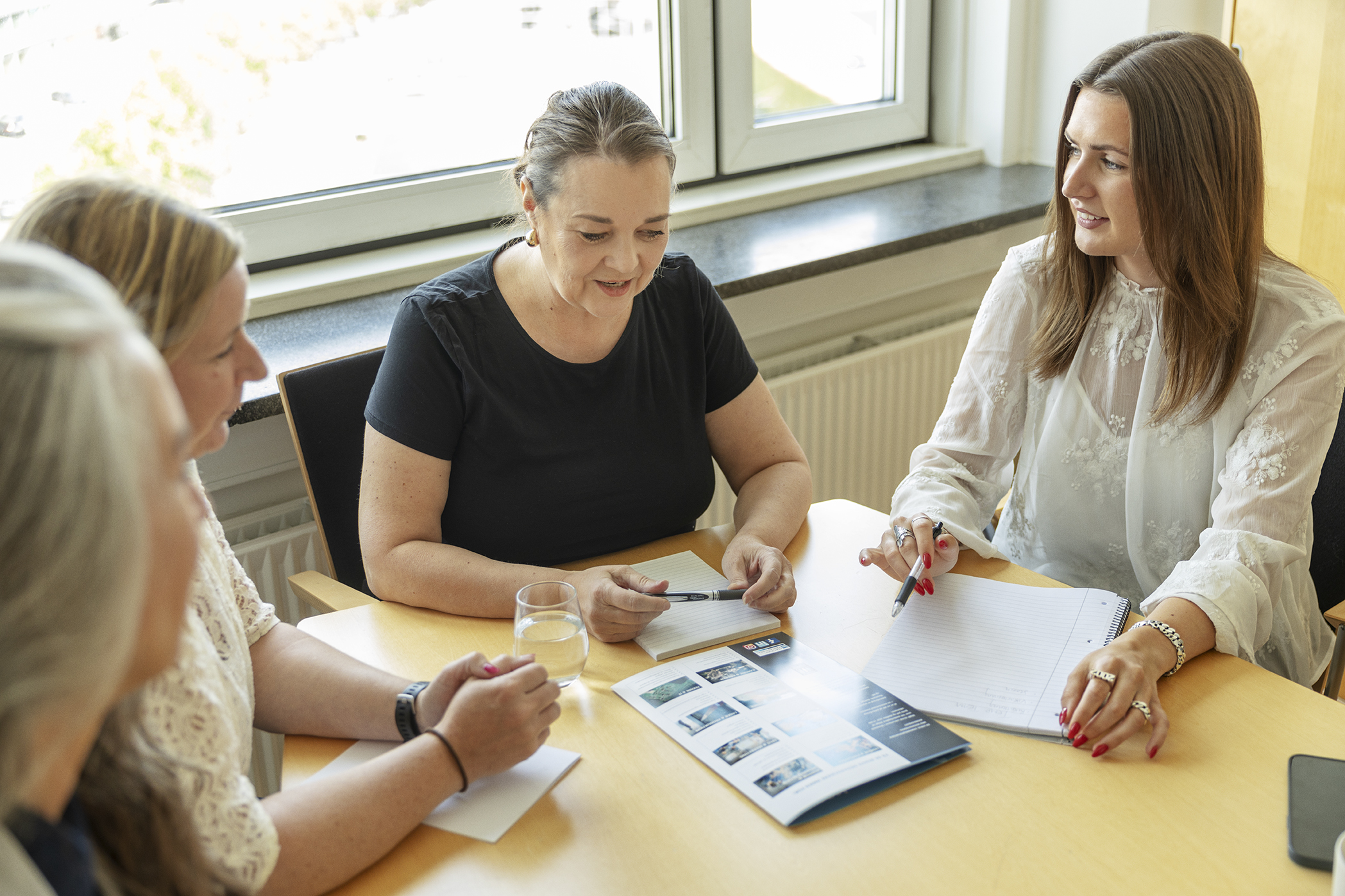 Fire kvinder holder et møde på et kontor i København med blokke og printmaterialer på bordet.